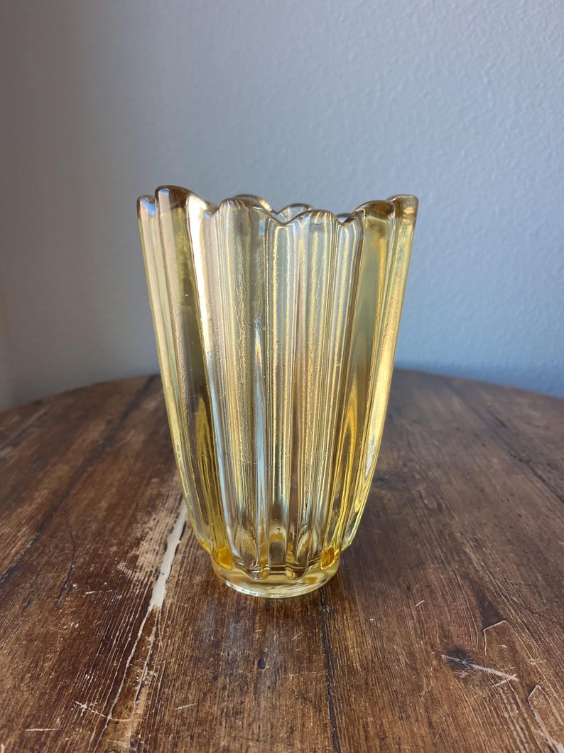 May include: A yellow glass vase with a fluted design. The vase has a wide mouth and a narrow base.