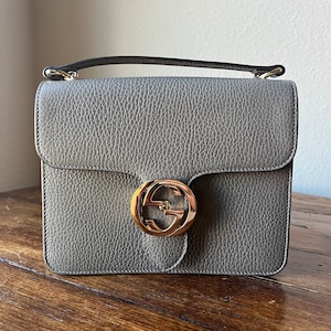 May include: A gray leather shoulder bag with a gold interlocking GG logo on the front.