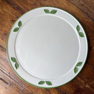 May include: A white ceramic serving platter with a green rim and green leaf designs around the edge.