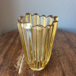 May include: A yellow glass vase with a fluted design and a scalloped rim.
