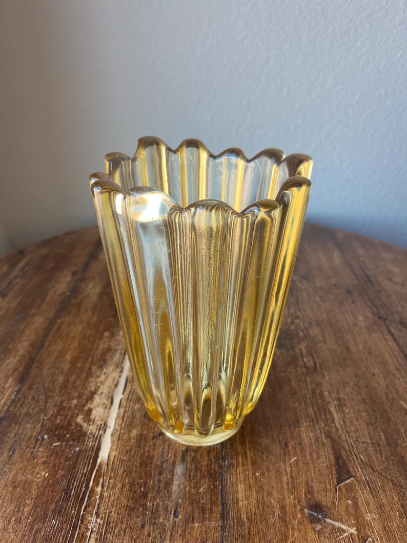 May include: A yellow glass vase with a fluted design and a scalloped rim.