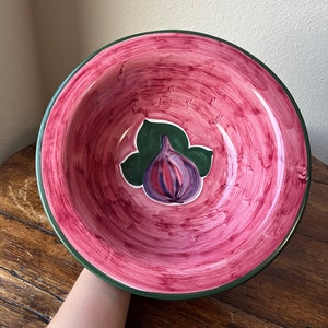 May include: A large, red ceramic bowl with a green rim and a painted fig design in the centre. The fig is purple with green leaves.