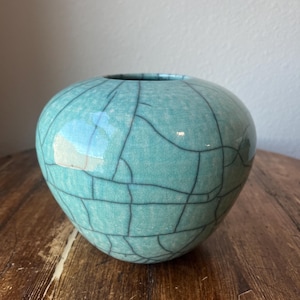 Op de afbeelding: Een teal keramische vaas met een craquelé glazuur. De vaas heeft een ronde, licht afgeplatte vorm.