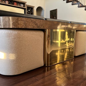 May include: A brown leather sectional sofa with a marble top and gold metal accents. The sofa has three matching ottomans with beige fabric upholstery.