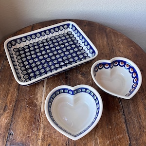 May include: A rectangular and two heart-shaped ceramic serving dishes. The dishes are white with a blue and white pattern. The rectangular dish has a repeating pattern of blue circles. The heart-shaped dishes have a blue border with a repeating pattern of blue and brown accents.
