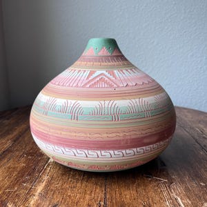 Könnte beinhalten: Eine handgefertigte, runde Vase mit breitem Boden und schmalem Hals. Die Vase hat eine Farbpalette aus Rosa, Grün und Beige mit geätzten geometrischen und linearen Mustern. Die Vase ist wahrscheinlich aus Keramik oder Ton.