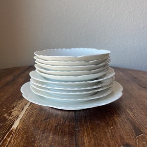 May include: A stack of white ceramic bowls with scalloped edges. The bowls are stacked on a wooden table.