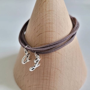 May include: A brown elastic bracelet with two silver charms, one with the letter "A" and the other with the letter "J".