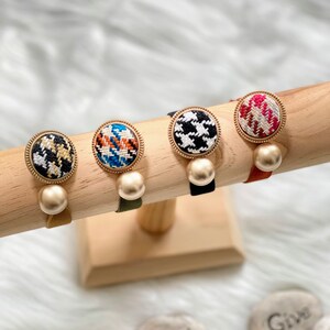 May include: Four hair scrunchies with different patterned fabric covered buttons and gold accents. Each scrunchie has a pearl-like bead attached to the button.