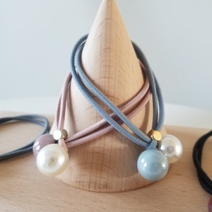 May include: Three hair ties with pearl and gold accents. The hair ties are in shades of blue, pink, and gray. The hair ties are displayed on a wooden cone.