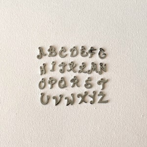 Agregue un dije de letra cursiva personalizado, un colgante con inicial o un dije de nombre de plata a su bolsa de joyas o regalo