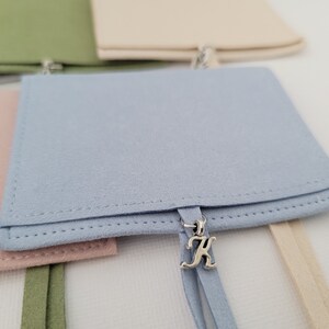 May include: A set of four small, fabric pouches with drawstrings. The pouches are in different colors: green, beige, pink, and light blue. The light blue pouch has a silver charm with the letter "K" on it.