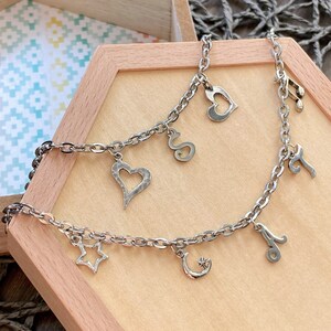 May include: A silver chain bracelet with multiple charms, including a heart, a star, a crescent moon, a musical note, and a letter 'S'.