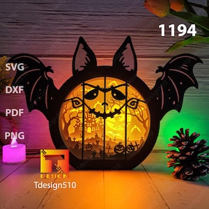 Op de afbeelding: Een zwarte houten vleermuis met een rond, verlicht gezicht. Het gezicht heeft een griezelige Halloween-scène met een spookhuis, bomen en pompoenen. De vleermuis wordt van achteren verlicht, waardoor een warme gloed ontstaat. De tekst "Tdesign510" en het nummer "1194" zijn zichtbaar op de afbeelding.