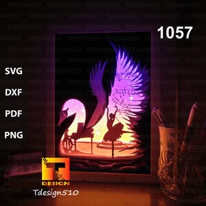 May include: A papercraft design featuring a swan with wings spread, a ballerina dancing on a piano, and musical notes. The design is illuminated from behind, creating a glowing effect. The design is labeled "1057" and is available in SVG, DXF, PDF, and PNG formats.