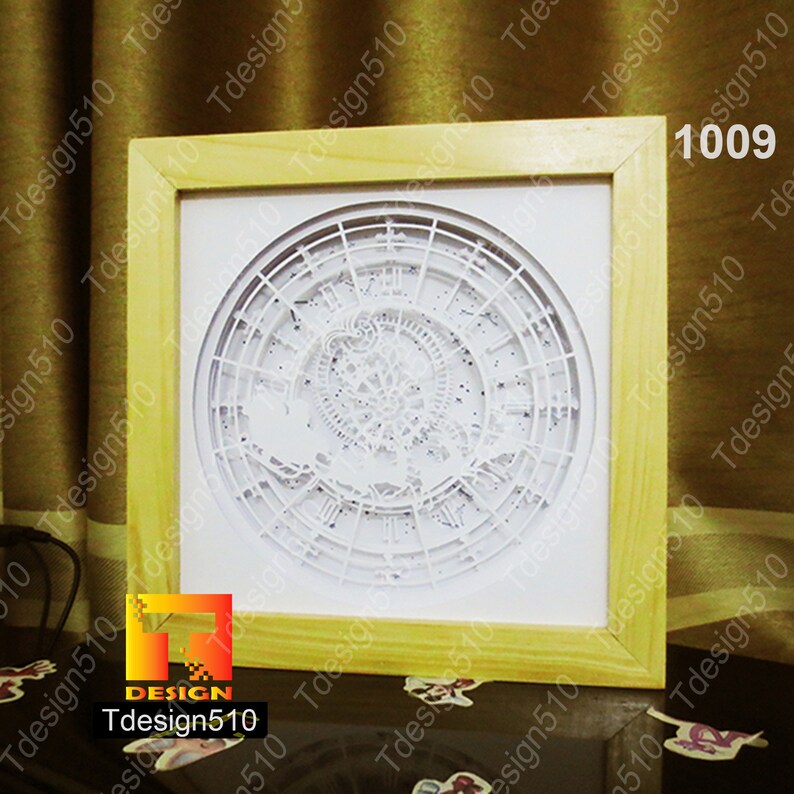 May include: A framed, layered paper art piece featuring a detailed clock design. The artwork is predominantly white, with intricate cut-out details, set within a light-colored wooden frame. The text "1009" is visible in the upper right corner.