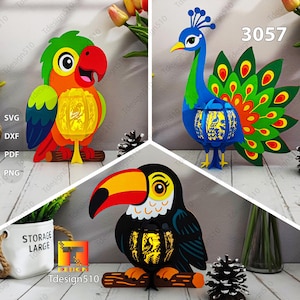 Puede incluir: Tres faroles decorativos con forma de pájaro: un loro, un pavo real y un tucán. El loro es rojo, naranja, verde y amarillo. El pavo real es azul, verde y naranja. El tucán es negro, amarillo y naranja. Cada uno está sobre una percha de madera.