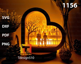 May include: A wooden heart-shaped lamp with a silhouette of a family standing in front of a cityscape with fireworks in the background. The lamp is lit and glows warmly. The text "1156" is visible in the upper right corner of the image.