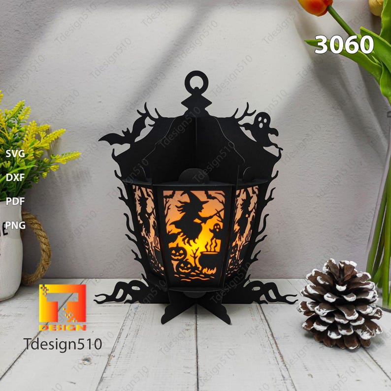 May include: A black Halloween lantern with a witch silhouette, bats, and ghosts. The lantern has a cutout design with a warm light inside, and the number 3060 is visible. The lantern is made of black material and has a decorative base.