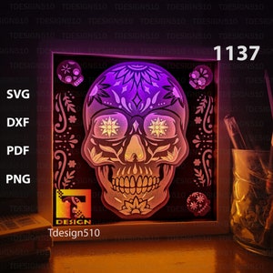 May include: A framed light-up design of a colourful sugar skull with floral details. The skull is illuminated with a purple and orange glow. The frame is white with the text "Tdesign510" and the number "1137" printed on it.