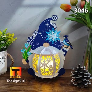 May include: A white, blue, and yellow papercraft gnome with a blue hat and a bird perched on its shoulder. The gnome is holding a bouquet of flowers and has a lantern with a snowflake design. The lantern is lit up with a warm yellow light. The image includes the text "3046".
