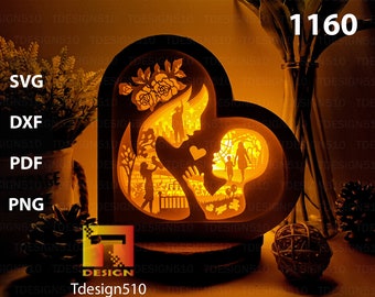 May include: A wooden heart-shaped lamp with a cutout design of a mother and child. The lamp is lit and glows warmly. The design includes a family scene with a mother, father, and child. The lamp is on a wooden base.