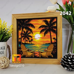 Puede incluir: Obra de arte enmarcada en madera que representa una escena de puesta de sol con palmeras, dos sillas de playa y un cielo naranja y amarillo vibrantes. La obra de arte tiene el texto "Tdesign510" y el número "2042" en el marco.