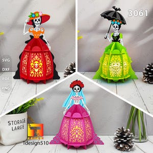 May include: Three colorful paper cut-out figures of Catrina, a traditional Day of the Dead icon. Each figure is a skeleton woman in a dress and hat, with intricate cut-out designs. The figures are red, green, and pink.