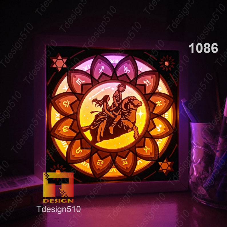 May include: A framed light-up paper art piece depicting the zodiac sign Aries. The artwork is illuminated with a warm yellow light, and the frame is white. The artwork is surrounded by a black background.