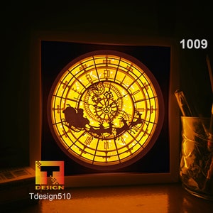 May include: A lit-up, framed, layered paper art piece featuring a clock design with a Santa Claus sleigh and reindeer silhouette. The clock face is yellow with intricate cut-out details. The text "1009" is in the upper right corner. The logo "T DESIGN Tdesign510" is in the lower left.