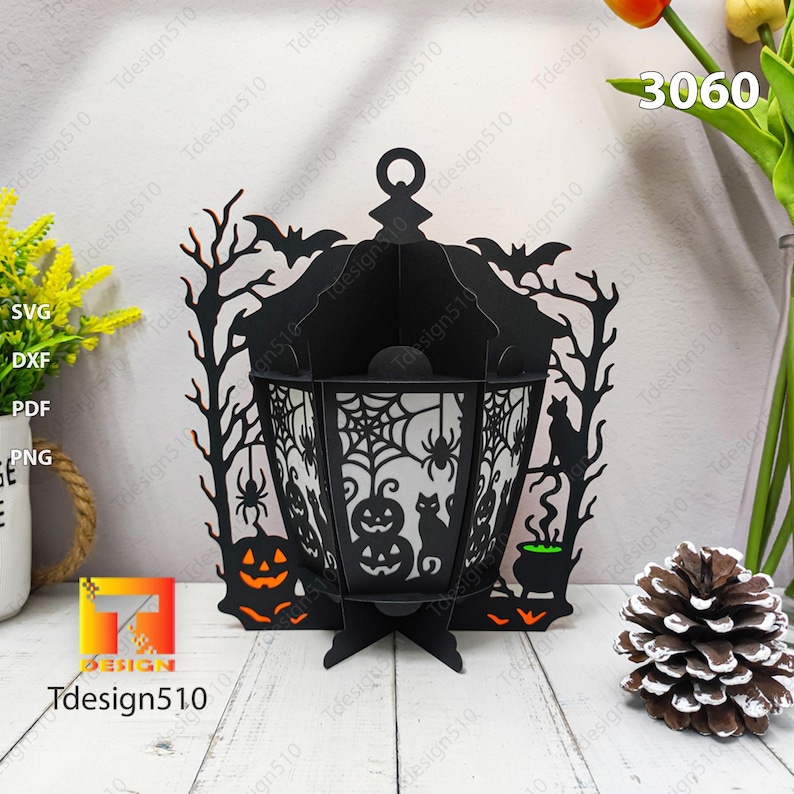 May include: A black Halloween lantern with intricate cut-out designs of bats, spiders, pumpkins, and a cat. The lantern has a handle and is supported by a base. The text "Tdesign510" is visible. The number "3060" is also visible.