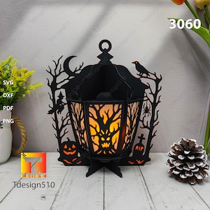May include: A black Halloween lantern with a spooky tree and pumpkin design. The lantern has a handle and is lit from within, creating a warm glow. The design includes a witch, spider, and crow.