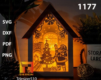 Op de afbeelding: Een witte houten huisvormige lichtgevende decoratie met een kerstmanfiguur, een kerstboom en een open haard binnenin. Het huis is van binnenuit verlicht, waardoor een warme gloed ontstaat. De tekst "1177" is zichtbaar in de rechterbovenhoek van de afbeelding.