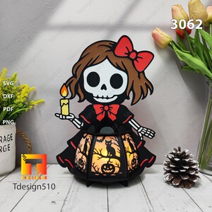 May include: A Halloween lantern with a skeleton girl design. The black lantern has cut-out designs of cats, pumpkins, and trees. The girl has a red bow and holds a candle. The image also includes the text "Tdesign510" and the number "3062".