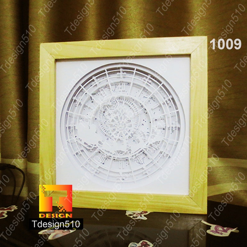 May include: A framed, layered paper art piece featuring a detailed clock design. The artwork is predominantly white, with intricate cut-out details, set within a light-colored wooden frame. The text "1009" is visible in the upper right corner.