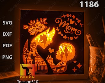 May include: A white wooden frame with a lit-up design inside. The design is a silhouette of a mother and child with the words "I Love You Mom" in a decorative font. The design is illuminated from behind, creating a warm glow.