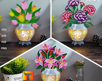 Könnte beinhalten: Drei lasergeschnittene Blumenarrangements in weißen Vasen mit einem Licht im Inneren. Die Blumen sind rosa, gelb und lila. Die Vasen haben ein dekoratives Design. Die Blumen sind Tulpen, Lilien und Nelken.