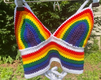 Puede incluir: Un top de crochet arcoíris con una tira de halter de crochet blanco y un lazo blanco en la parte inferior.