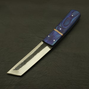 May include: A handcrafted knife with a blue wooden handle and a polished steel blade. The handle features a copper accent and white dot inlays. The blade has a straight edge and a slightly angled tip. The knife is designed for cutting.