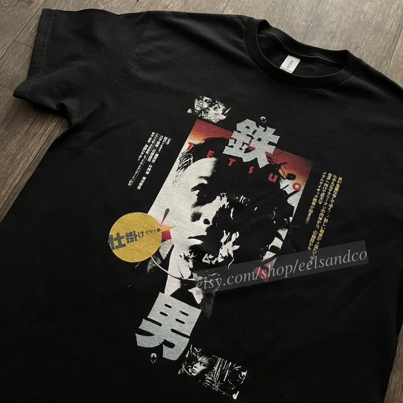 Puede incluir: Camiseta negra con un dise&ntilde;o gr&aacute;fico que incorpora texto japon&eacute;s y un retrato. El dise&ntilde;o incluye la palabra "Tetsuo" y otros caracteres japoneses. Tambi&eacute;n hay un c&iacute;rculo amarillo con texto japon&eacute;s.