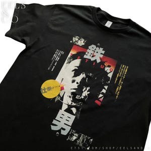 Puede incluir: Camiseta negra con un dise&ntilde;o gr&aacute;fico que presenta texto japon&eacute;s y un retrato. El dise&ntilde;o incluye acentos rojos, blancos y amarillos. La palabra "Tetsuo" es visible.