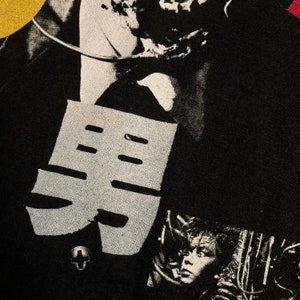 Puede incluir: Camiseta negra con un dise&ntilde;o gr&aacute;fico que presenta un car&aacute;cter japon&eacute;s estilizado y un collage de im&aacute;genes en blanco y negro. El dise&ntilde;o incluye un elemento en forma de cruz y un retrato.