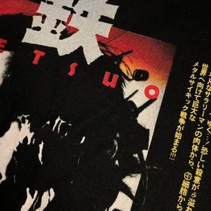 Puede incluir: Camiseta negra con gr&aacute;ficos y texto japon&eacute;s y un dise&ntilde;o de puesta de sol rojo y naranja. El texto incluye la palabra "TSU" en blanco y caracteres japoneses. La camiseta presenta una ilustraci&oacute;n estilizada con texto japon&eacute;s.