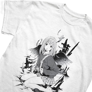 Puede incluir: Ilustración en blanco y negro de una joven con el pelo largo y una cámara, que lleva un jersey y una falda. Está de pie frente a una gran criatura alada oscura. La imagen está en una camiseta blanca.