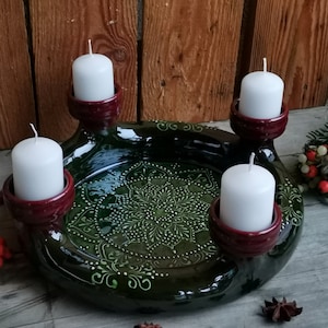 Puede incluir: Un candelabro de cerámica hecho a mano con cuatro velas blancas. La base verde oscuro presenta un diseño floral detallado y cuatro portavelas burdeos. Una pieza decorativa para el hogar.