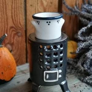 Peut inclure: Un chauffe-cire en céramique noire avec trois pieds et un pot en céramique blanche avec une bordure bleue sur le dessus. Le pot a une petite poignée de chaque côté et des points bleus sur le devant.
