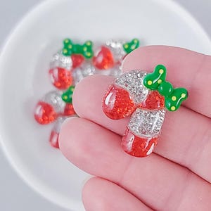 May include: A close-up of a red and white candy cane charm with a green bow. The charm is covered in glitter and rhinestones.