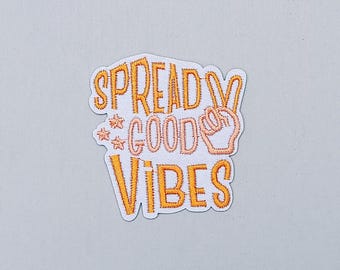 May include: White embroidered patch with the text "Spread Good Vibes" in orange and peach. The patch features a peace sign with a finger pointing up.