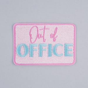 Puede incluir: Un parche rectangular rosa bordado con las palabras "Out of OFFICE" en hilo azul claro y rosa. El parche tiene un borde rosa y está sobre un fondo gris claro. El texto está en una fuente de escritura.