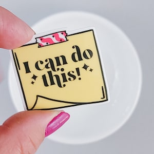 Könnte beinhalten: Ein gelber Aufkleber mit schwarzem Rand und dem Text "I can do this!" in schwarzen Buchstaben. Der Aufkleber hat ein rosa-weiß gestreiftes Klebeband oben.